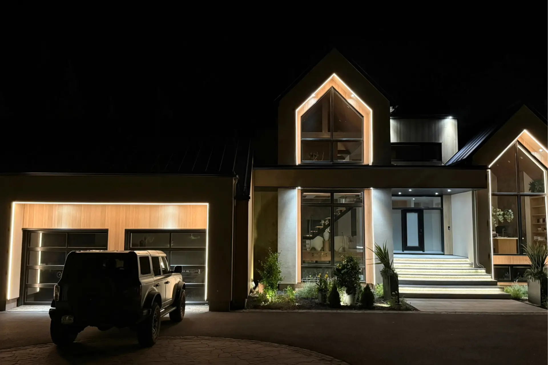 Modern home at night with warm white architectural lighting on gables and garage