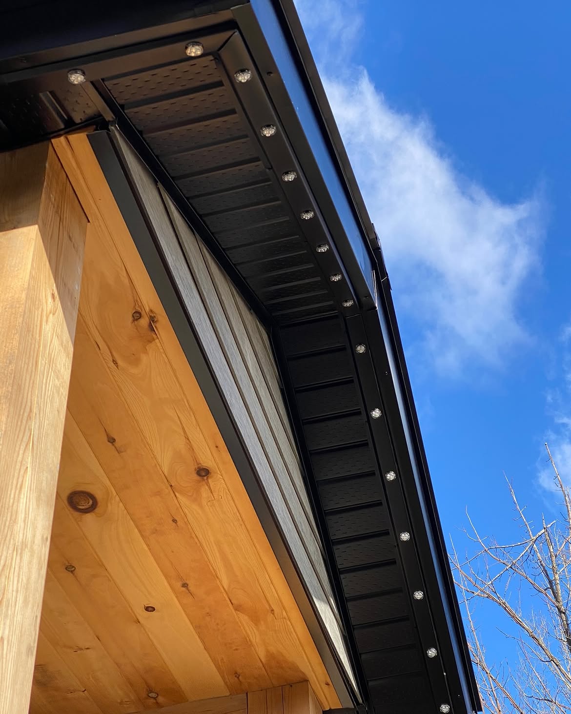 Black permanent lighting track turning a corner above warm wood siding